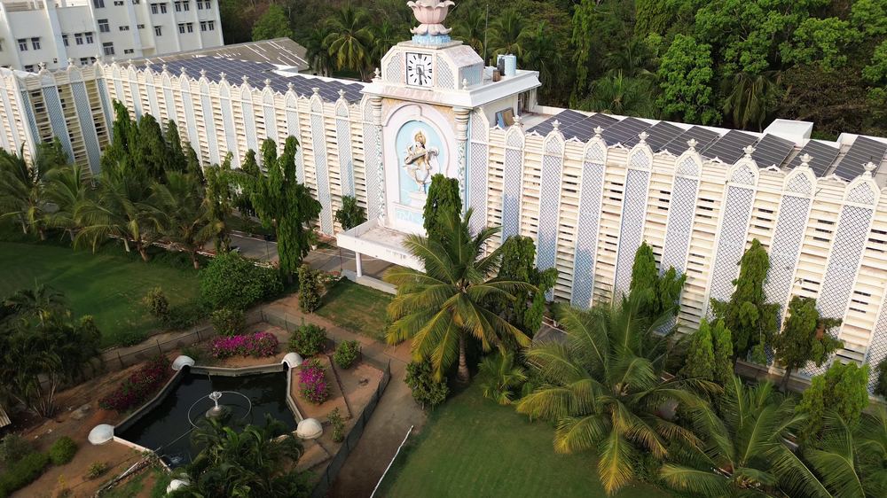 The Institute's main building amid palms and flowering gardens, from above (Pink.lotus.deva, Wikimedia Commons · CC0).