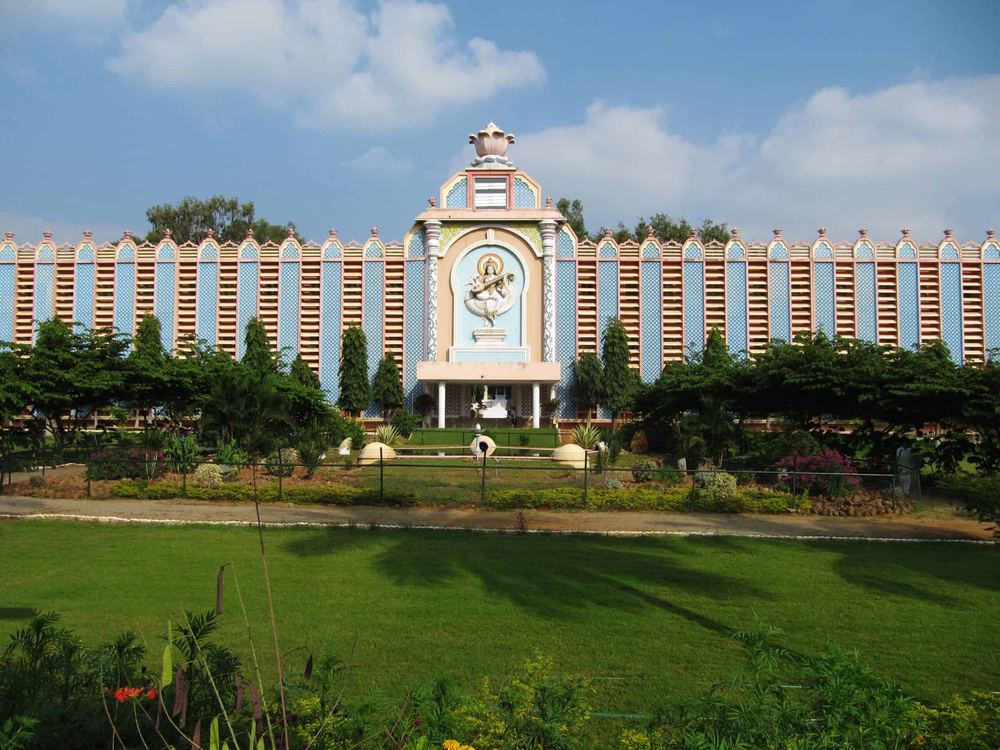 Sri Sathya Sai Institute of Higher Learning — the blue-and-white colonnade behind its gardens (DigitalKush, Wikimedia Commons · CC0).